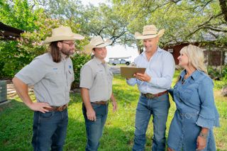 Four people discussing paperwork on a clipboard in an outdoor rural Texas ranch.