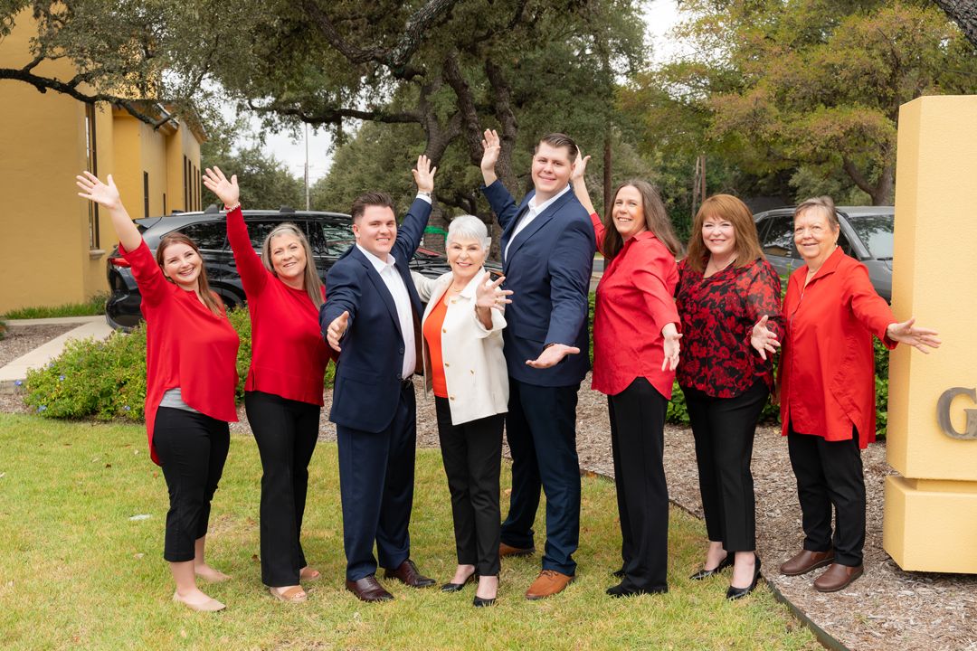 Seven colleagues in red outfits strike a fun pose with arms outstretched outdoors.