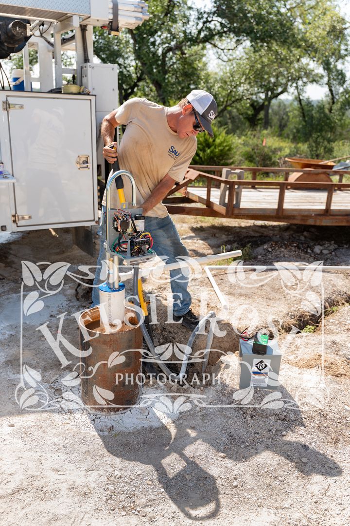 Worker in branded tan shirt and cap works on equipment at an outdoor construction site.