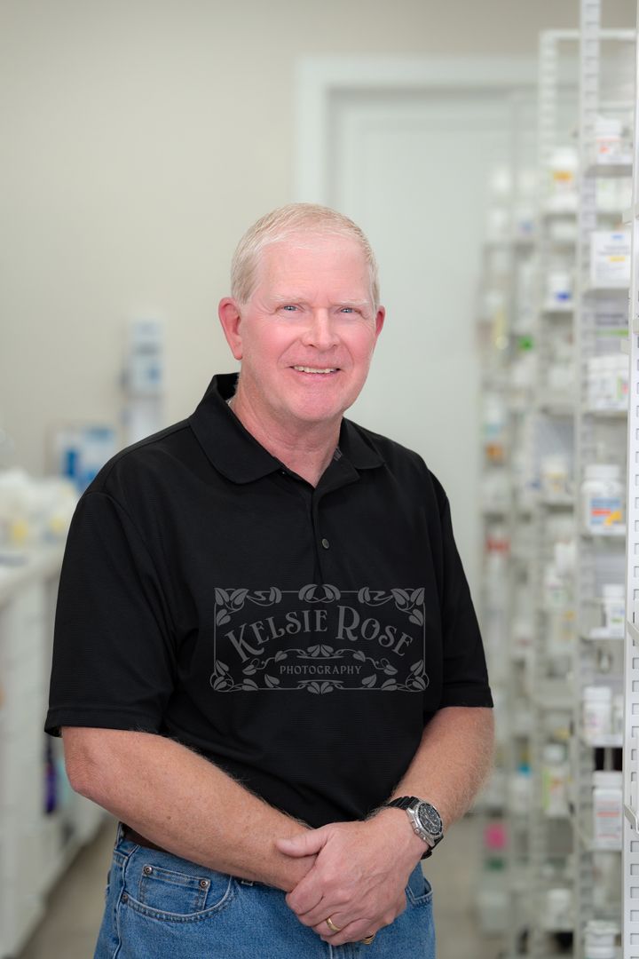 Male pharmacy employee in black polo shirt and jeans posing in a well-stocked pharmacy shelves.