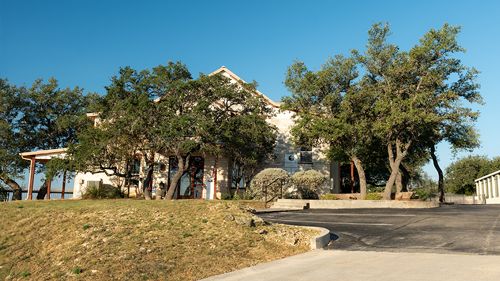 Large two-story Texas Hill Country office surrounded by mature oak trees with driveway.