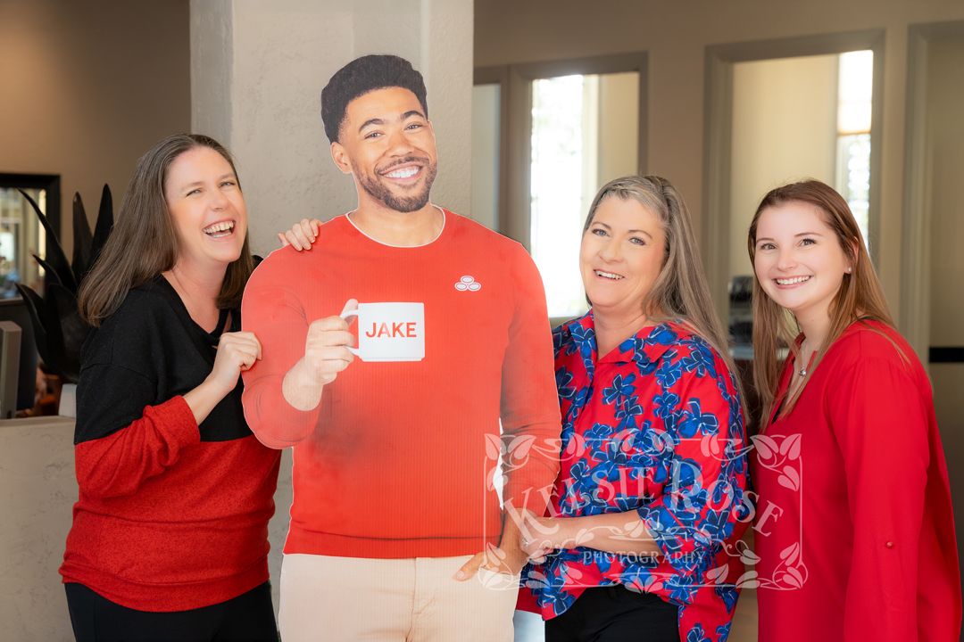 Four people smiling and posing with a cardboard cutout labeled Jake at an indoor event.