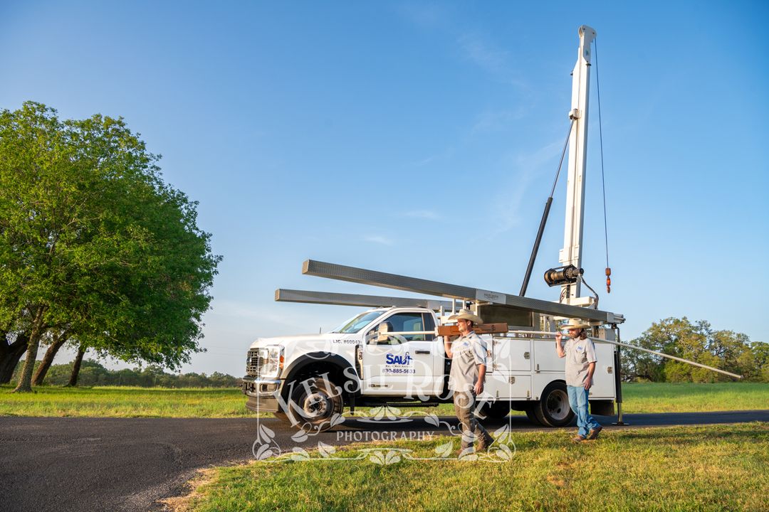 Water well service truck with extended crane on ranch road with technician working outdoors.