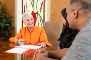 Elderly woman in orange top showing documents with a couple across the table at a meeting.