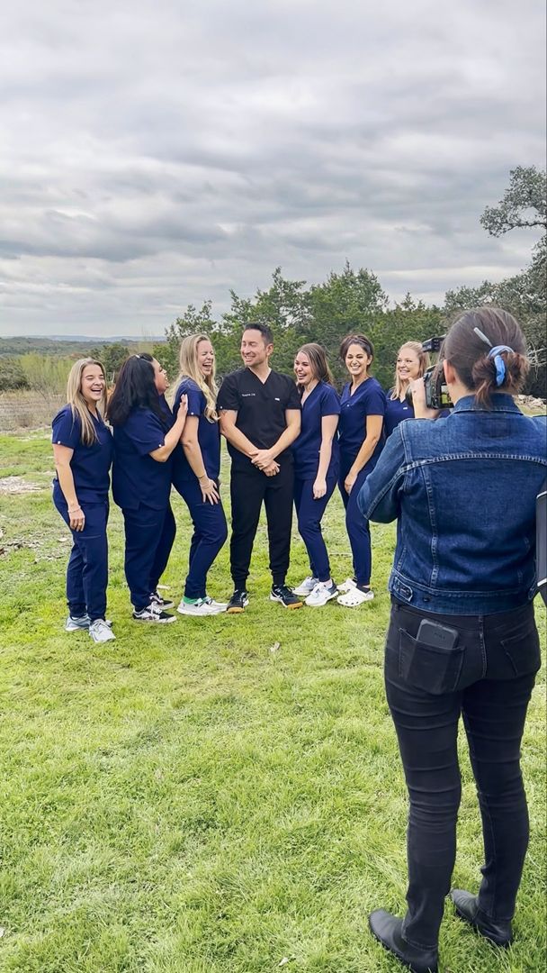 Healthcare team in navy scrubs posing for group photo outdoors on green grass with cloudy sky background.