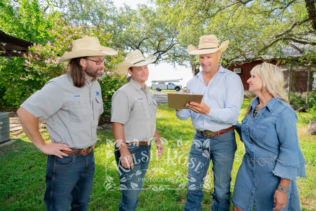 Four people including two workers in cowboy hats reviewing a documents on a clipboard outdoors on a ranch in Texas.