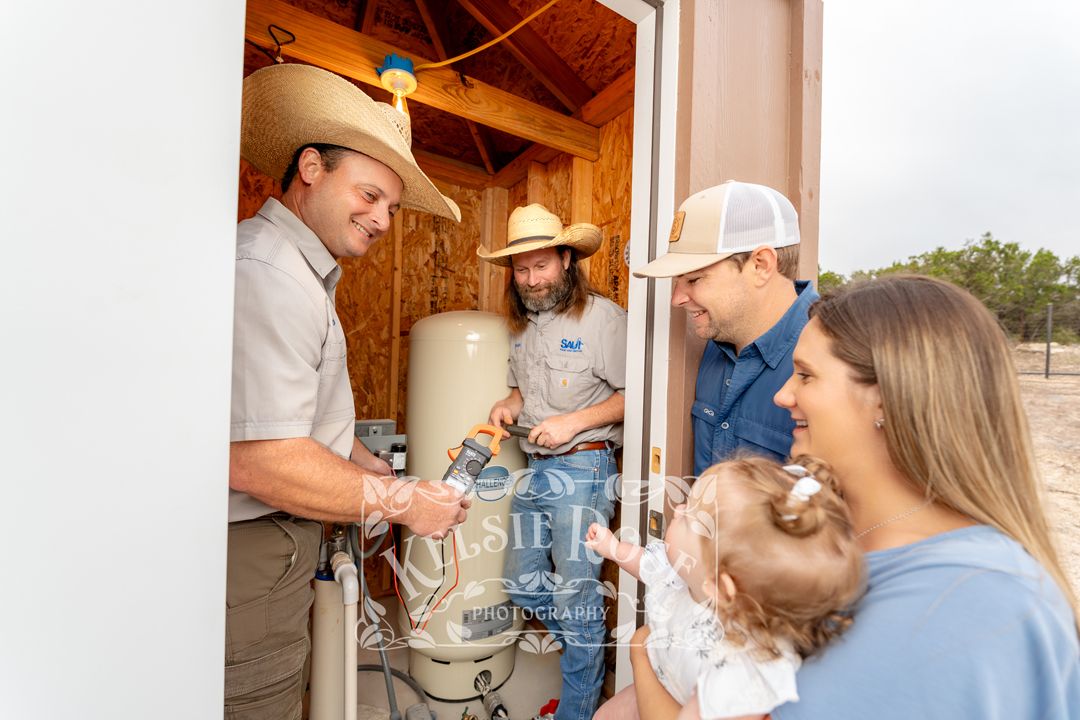 Four adults and a baby inspecting a newly installed well inside a well building in Texas.