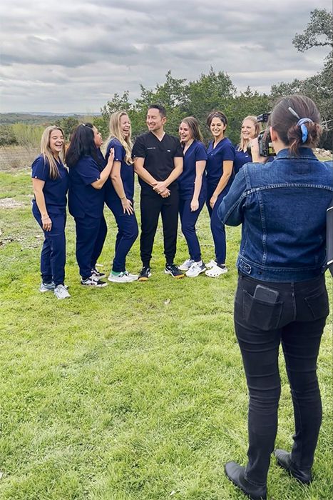 Behind the scenes of photographer taking outdoor group photo of medical team in navy scrubs in the Texas Hill Country.