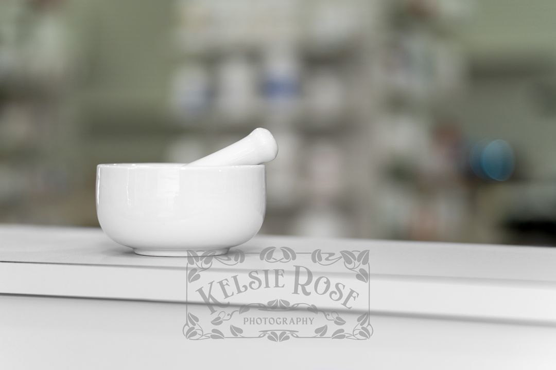 White mortar and pestle on pharmacy counter with blurred medication shelves in background.