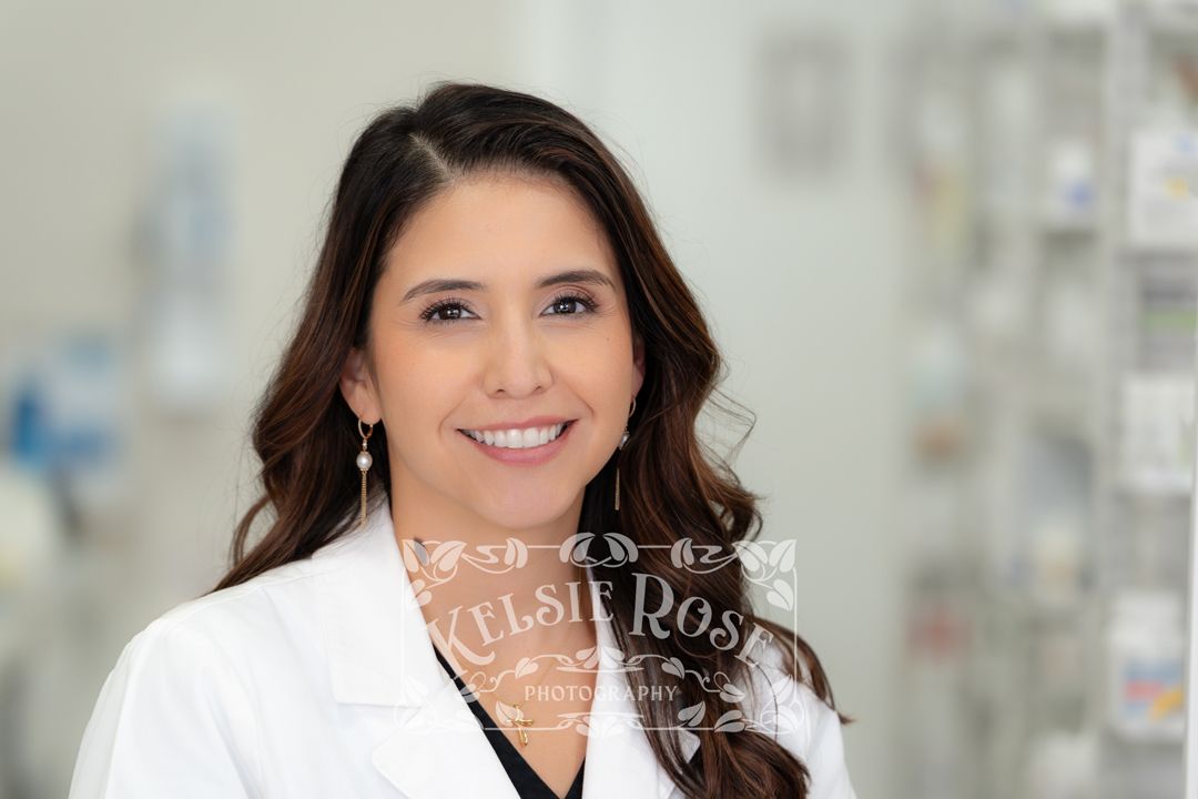 Headshot of a smiling female pharmacist in a white coat inside a pharmacy.