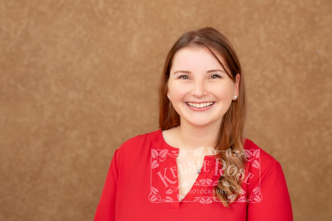 Young woman with brown hair and braces smiling warmly in red top, professional portrait photography.