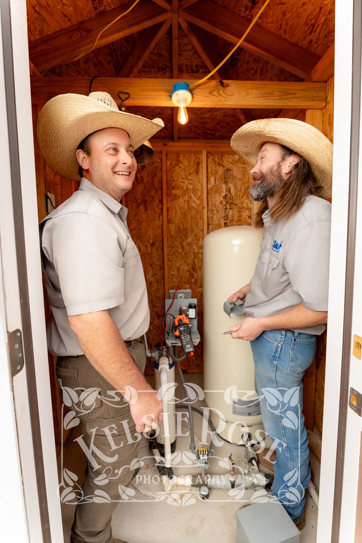 Two water well service technicians in cowboy hats inspecting a water tank inside a well building in Texas.