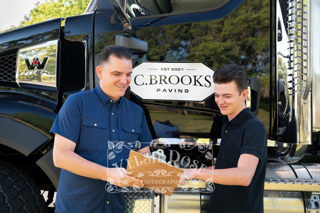 Two men reviewing documents together in front of a C. Brooks Paving company truck.
