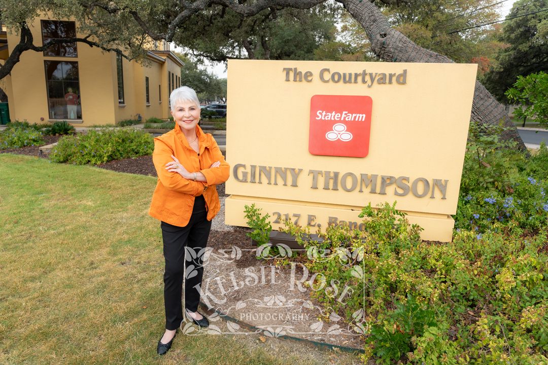 Woman in orange jacket poses by State Farm agent Ginny Thompson sign at The Courtyard office location.