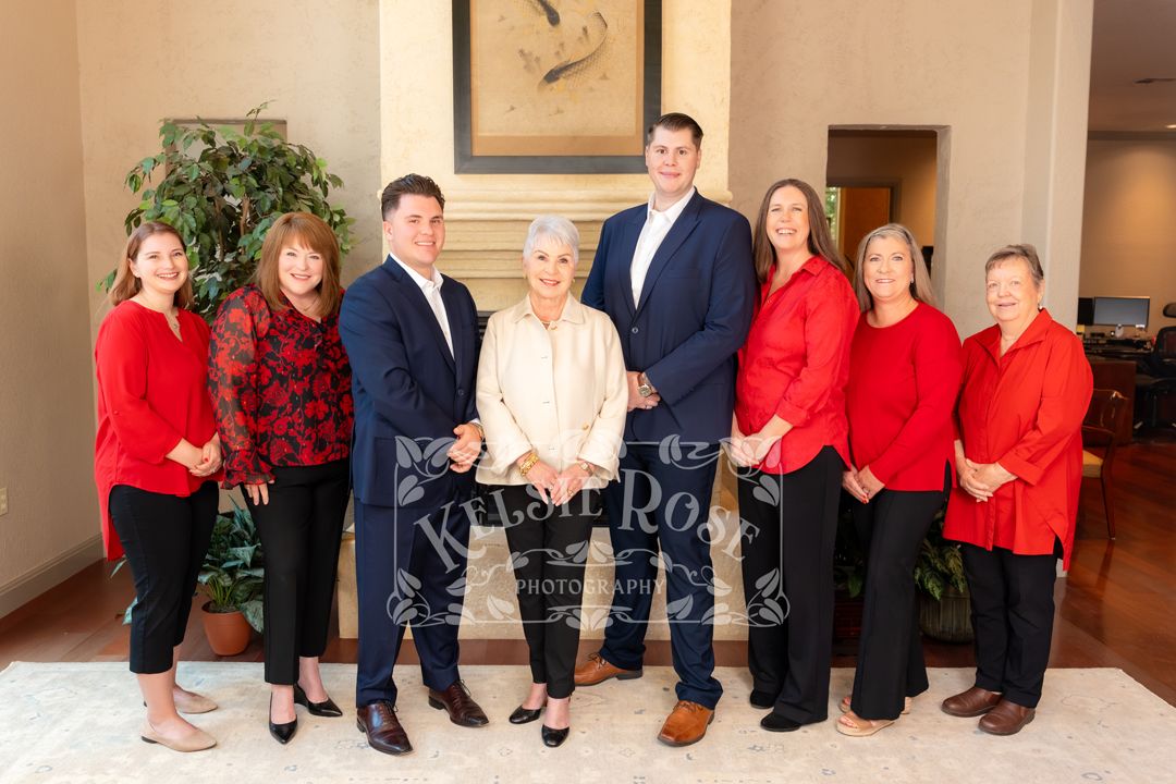 Group of nine professionals in red and dark attire posing together in an elegant lobby setting.