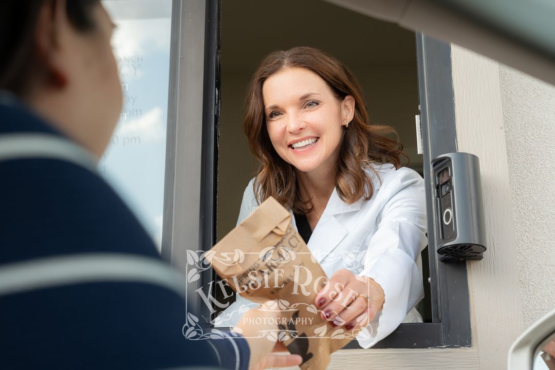 Smiling female pharmacist handing medication bag through drive-through window to customer.