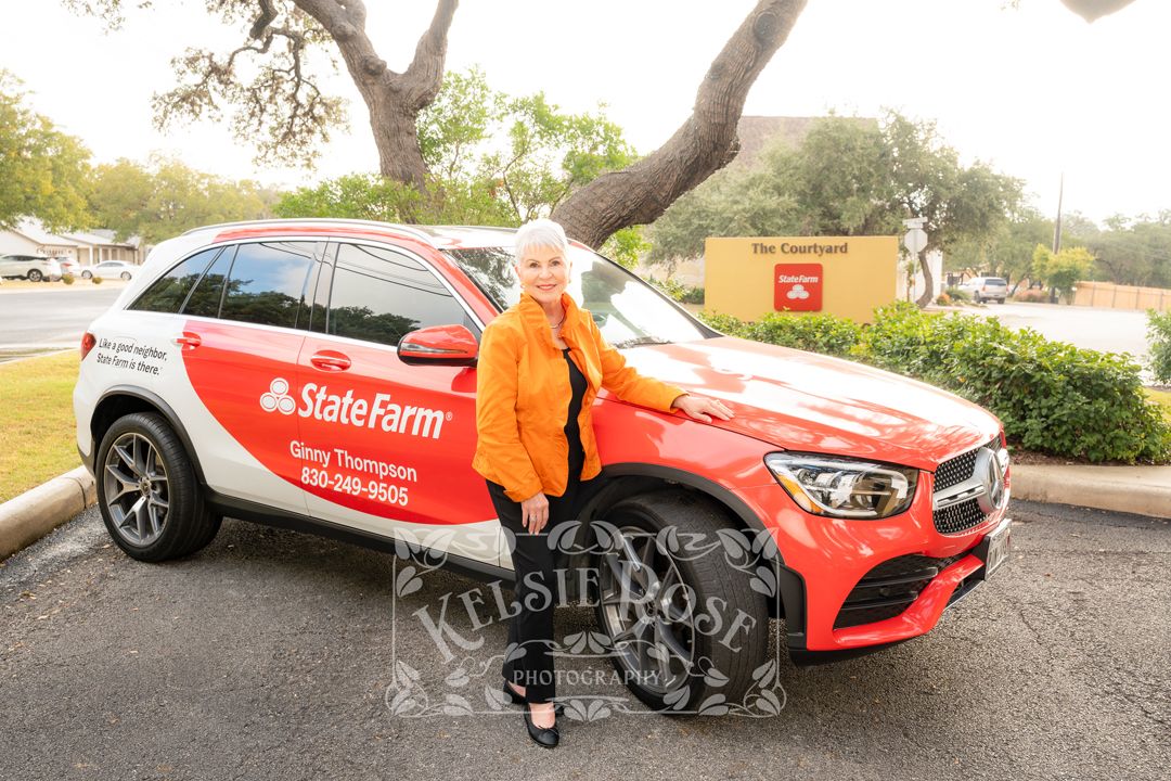 Woman posing beside a red State Farm branded Mercedes SUV belonging to Ginny Thompson in a parking lot.
