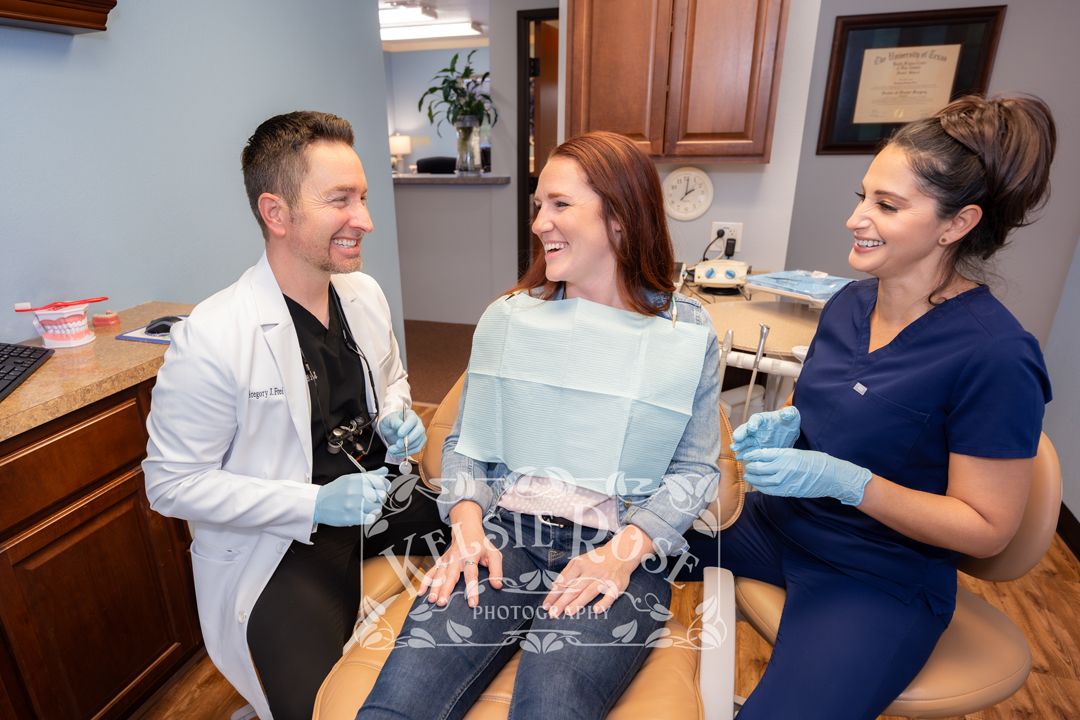 Male dentist and female dental assistant laughing with a cheerful red-haired patient in dental chair.
