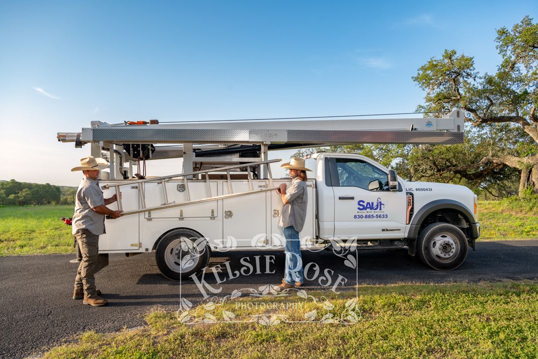 Two Saur Water Well Service employees removing ladder from white service truck outdoors.