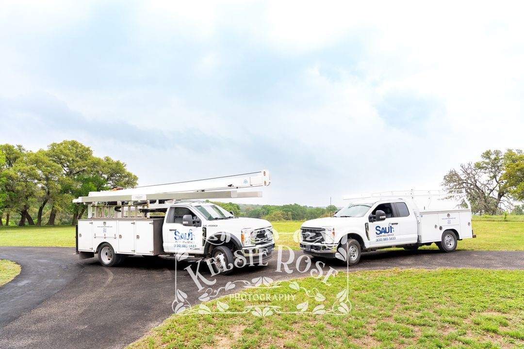 Two Saul Water Well Service branded work trucks parked on rural Texas ranch road with oak trees.