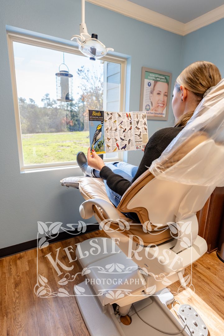 Dental patient relaxing in chair reading bird identification brochure with scenic window view that has bird feeder.
