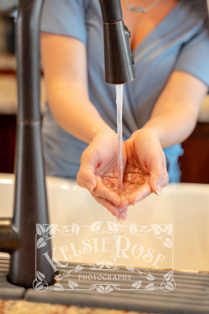 Close-up of woman's hands collecting water from a black kitchen faucet.
