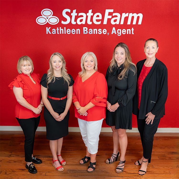 Five women posing together in front of a red State Farm Kathleen Banse Agent office wall.