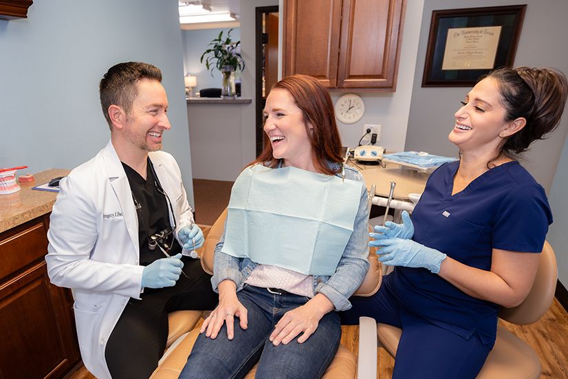 Dentist and dental assistant consulting with a happy female patient in a dental office.
