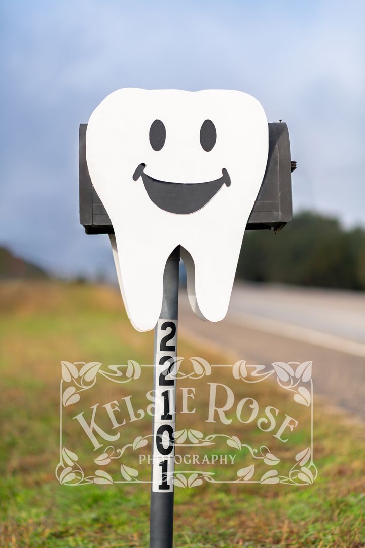 Unique tooth-shaped mailbox with a smiley face displaying address number along a roadside.
