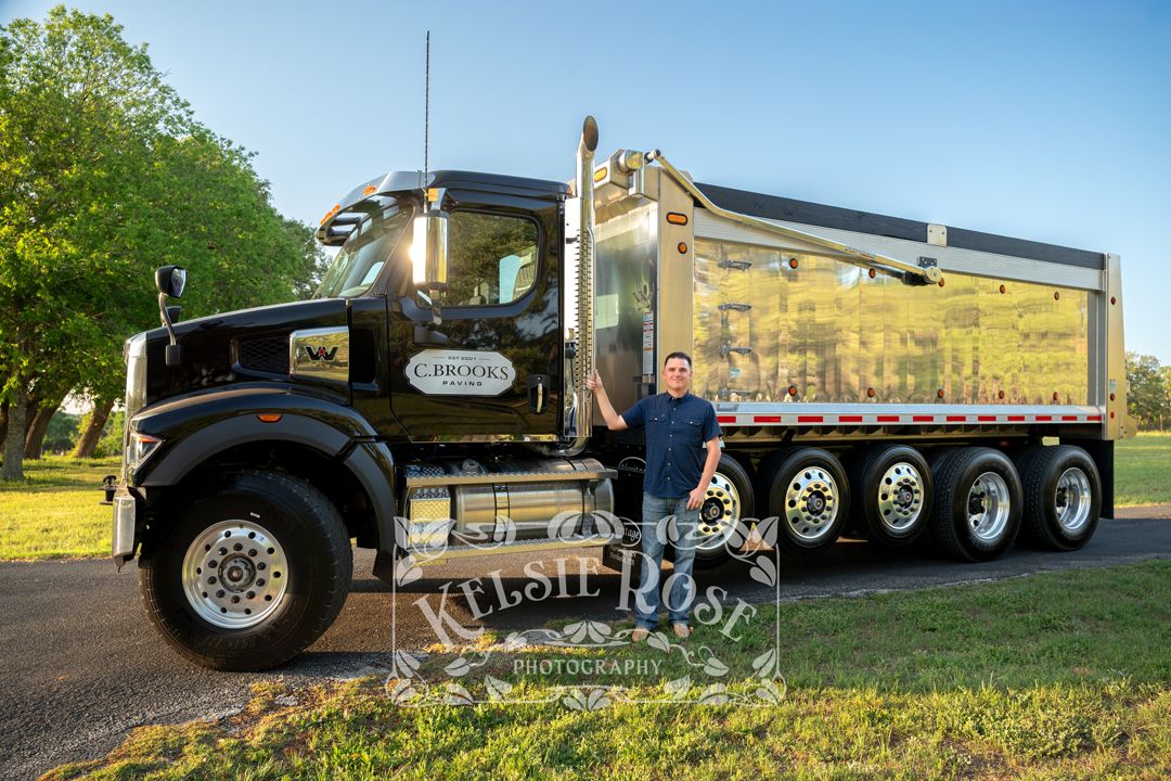 Man posing proudly next to a black and chrome heavy-duty dump truck outdoors.