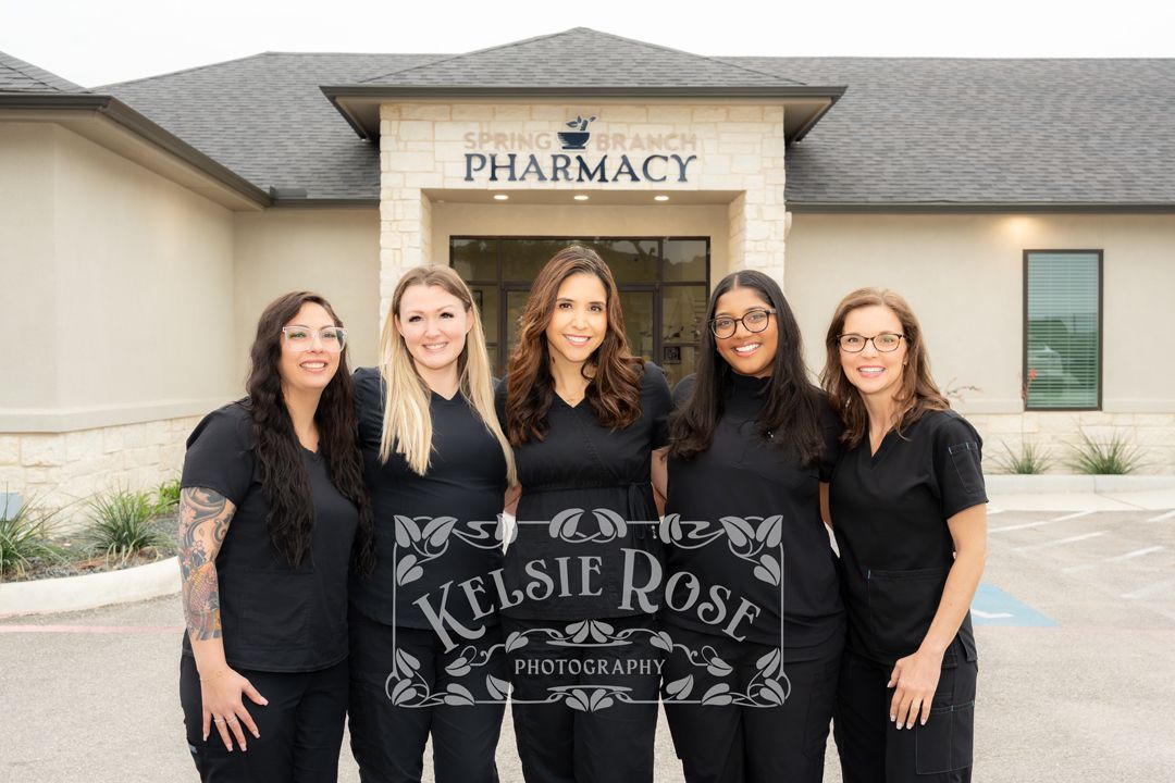Five pharmacy staff members in black scrubs pose in a group photo outside a pharmacy.