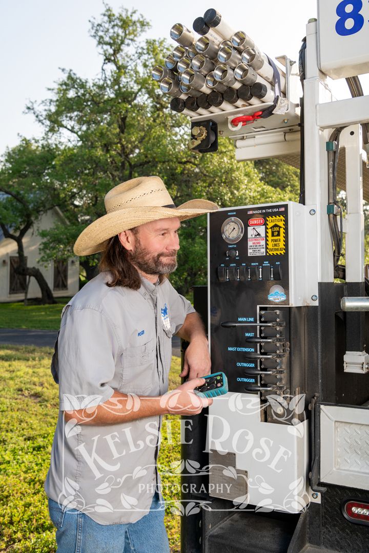 Male water well technician in cowboy hat operating control panel on service truck outdoors.