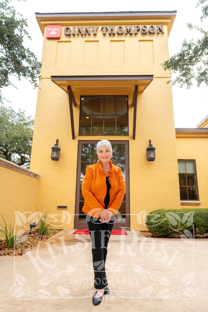 Woman in orange jacket poses confidently outside Ginny Thompson real estate office building.