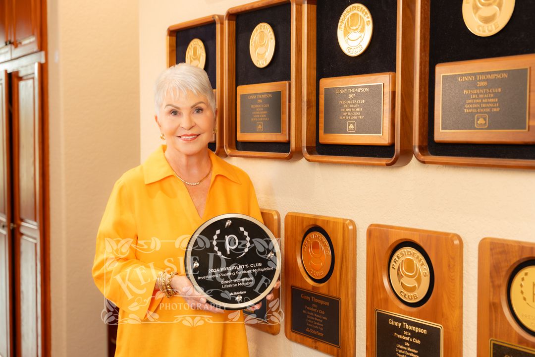 Elegant woman in yellow blazer holding award plaque beside wall of achievement awards in professional office.