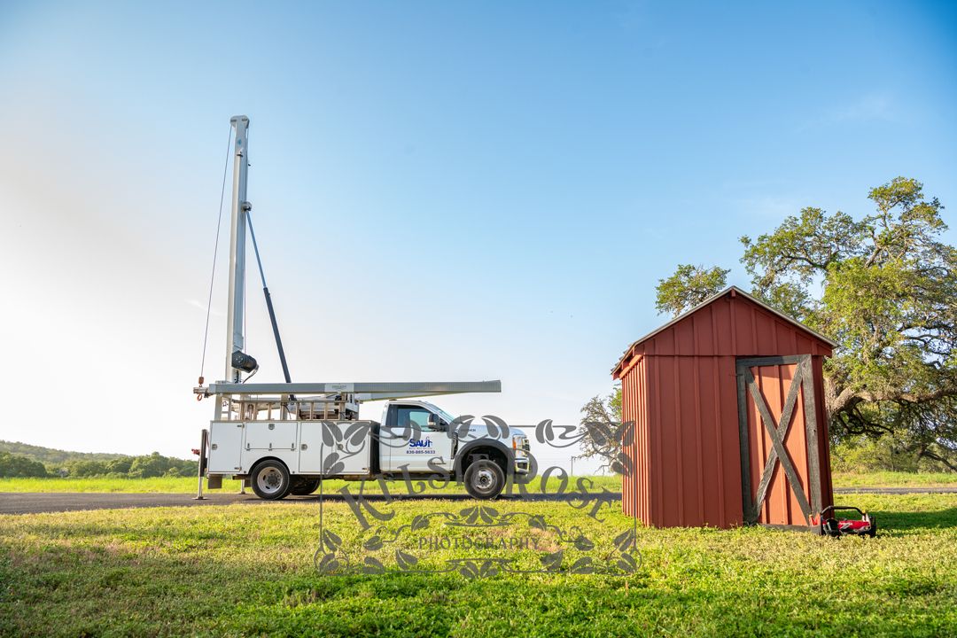 Saur Water Well Service truck with crane up parked near red well building on ranch.