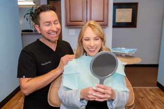 Dentist and smiling female patient admiring her new smile in a handheld mirror at dental office.