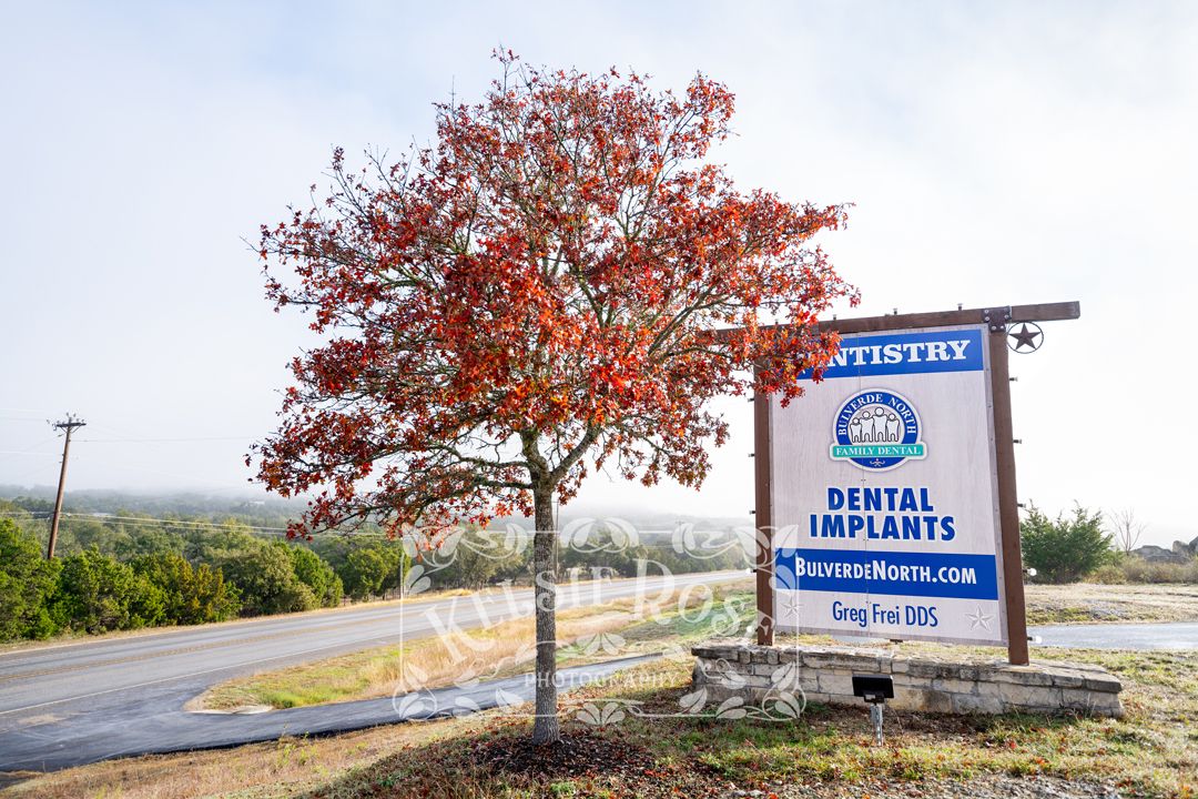 Roadside dentistry sign advertising dental office with a red-leafed tree.