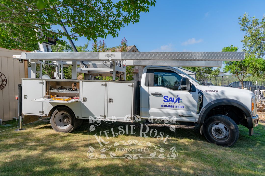 Water well service company truck parked on green lawn in backyard under shady trees.