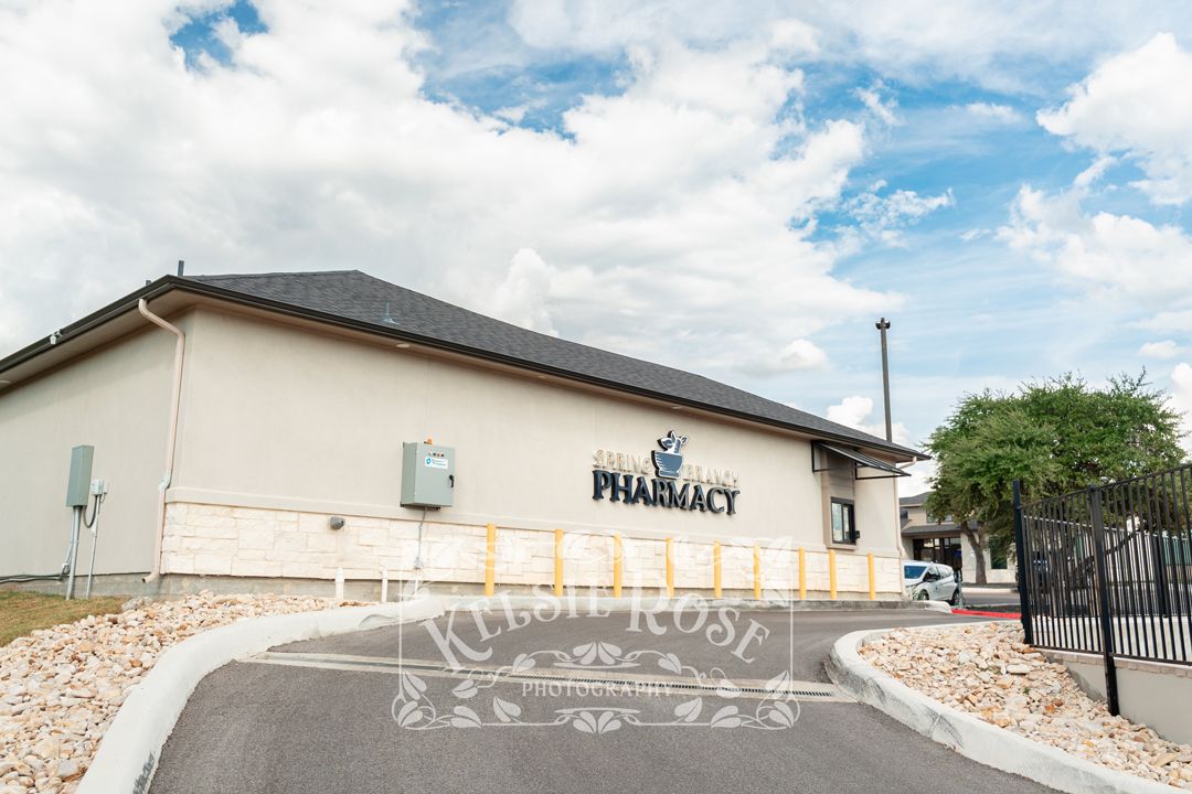 Exterior view of Spring Branch Pharmacy building with delivery window and paved driveway under cloudy sky.