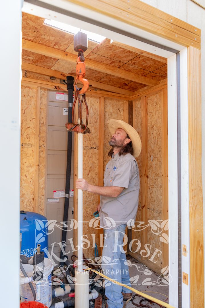 Bearded worker in straw hat pulling water pipe inside wooden well building.