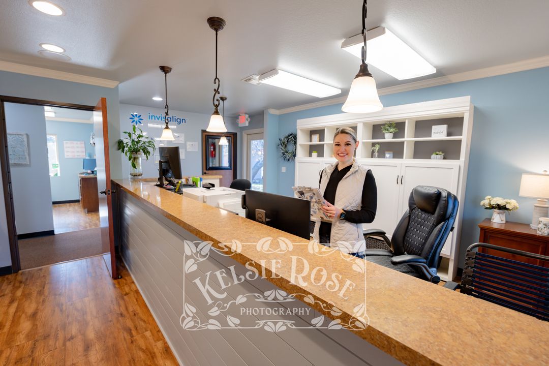 Professional female receptionist smiling at welcoming dental office front desk.