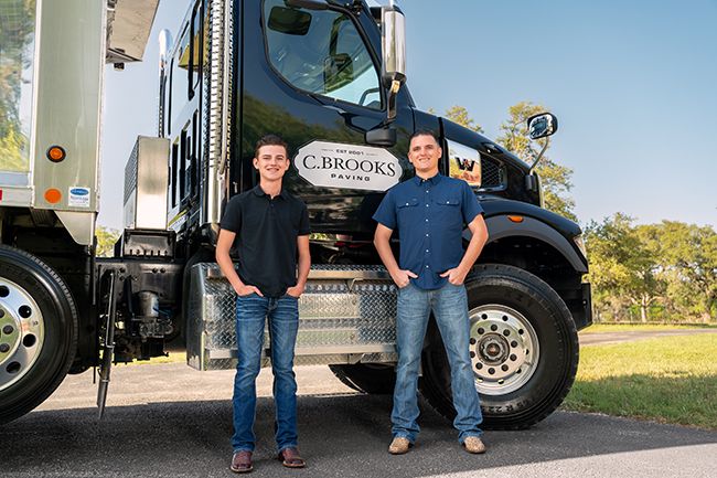Father and son stand proudly in front of a C. Brooks Paving branded commercial truck outdoors.