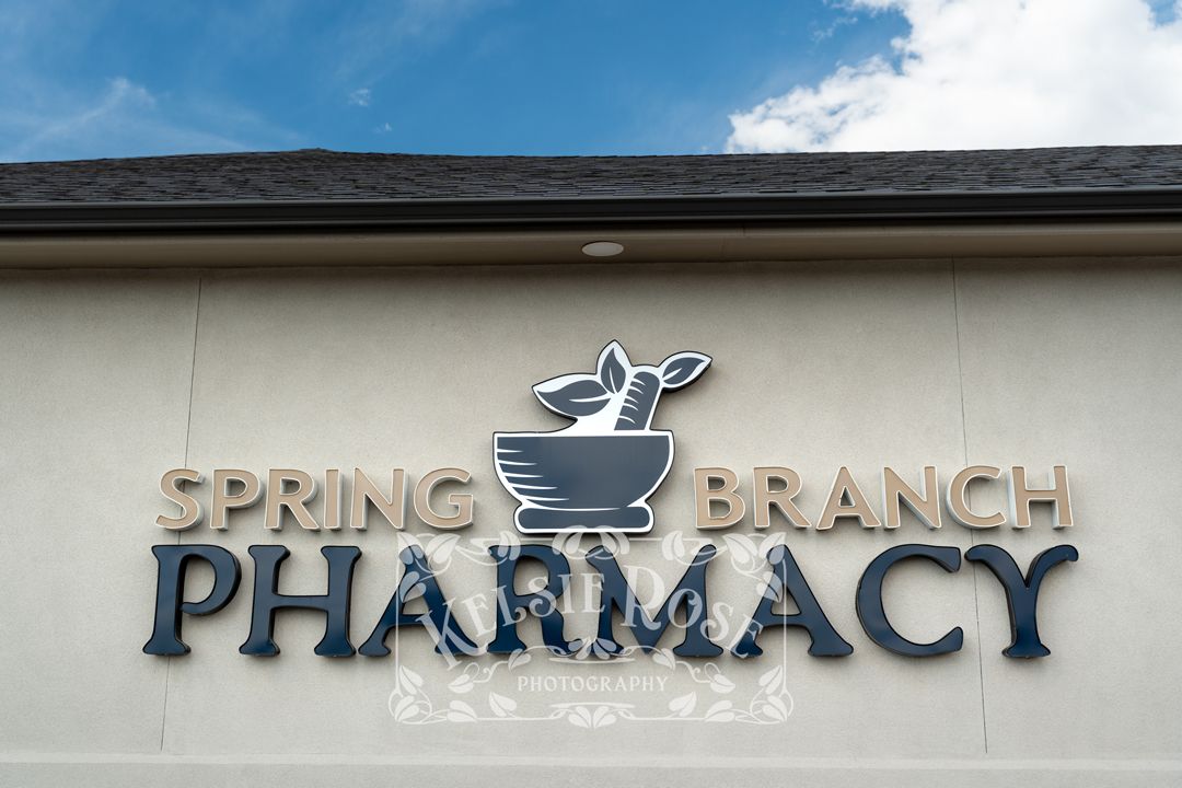 Close-up of Spring Branch Pharmacy sign featuring mortar and pestle logo on beige building exterior.