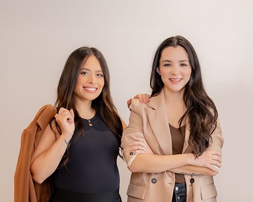 Two young women in blazers posing confidently against a white background.