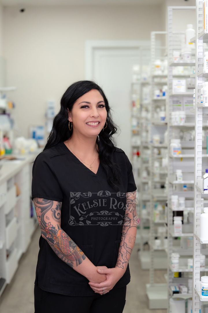Female pharmacy technician in black scrubs standing in a pharmacy shelves.