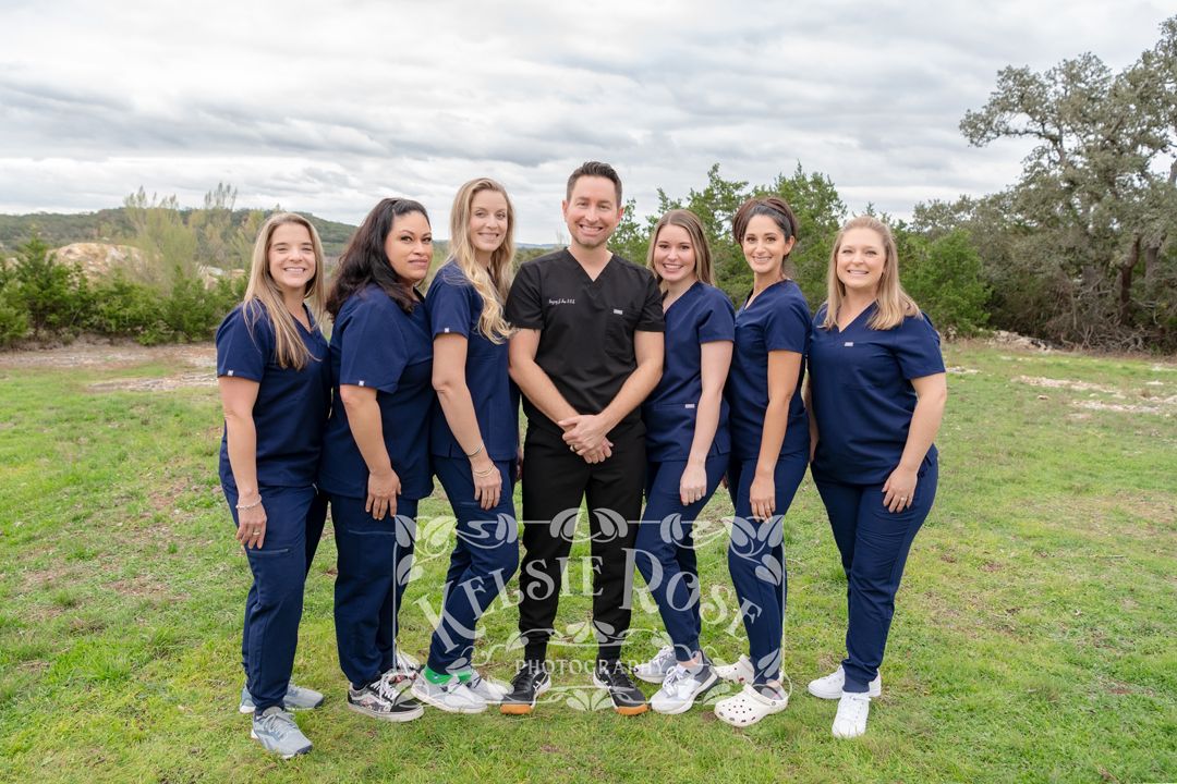 Seven dental team members in navy scrubs pose together outdoors on a cloudy day.
