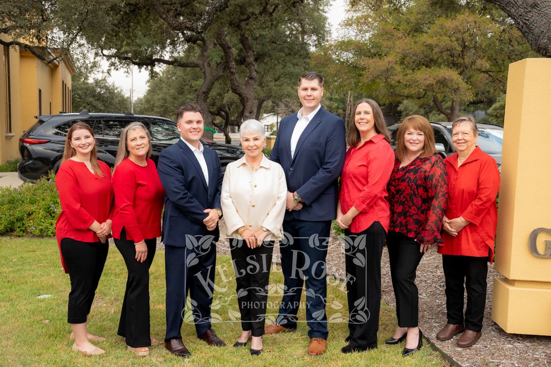 Group of seven professionals in red and blue attire posing outdoors near a yellow sign.