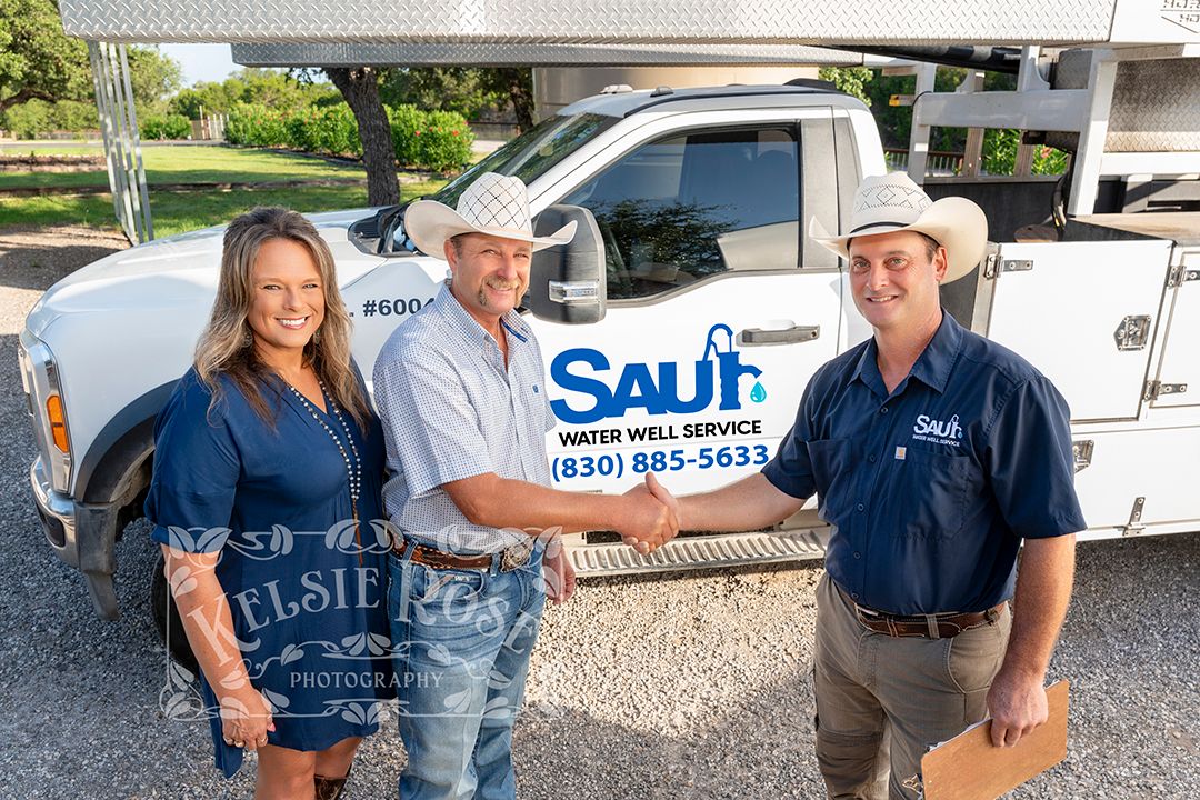Business owner shaking hands with clients in front of a Saur Water Well Service truck in an outdoor setting.