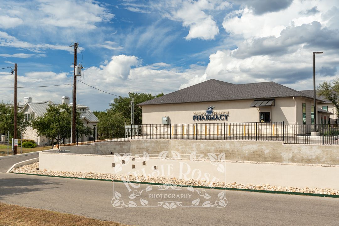 Exterior street view of Spring Branch Pharmacy building with driveway under a cloudy blue sky.
