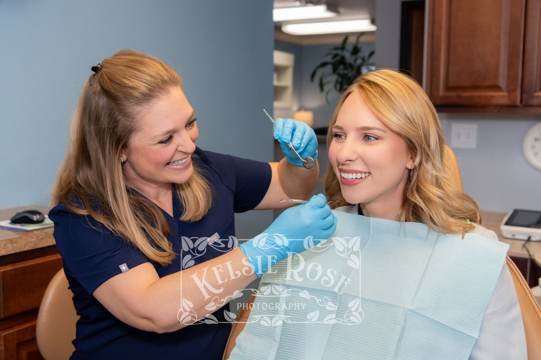 Friendly dental hygienist examining smiling female patient in dental chair.